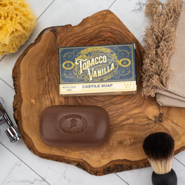 Single bar of tobacco vanilla soap sitting on slab of tree with shaving brush and towel