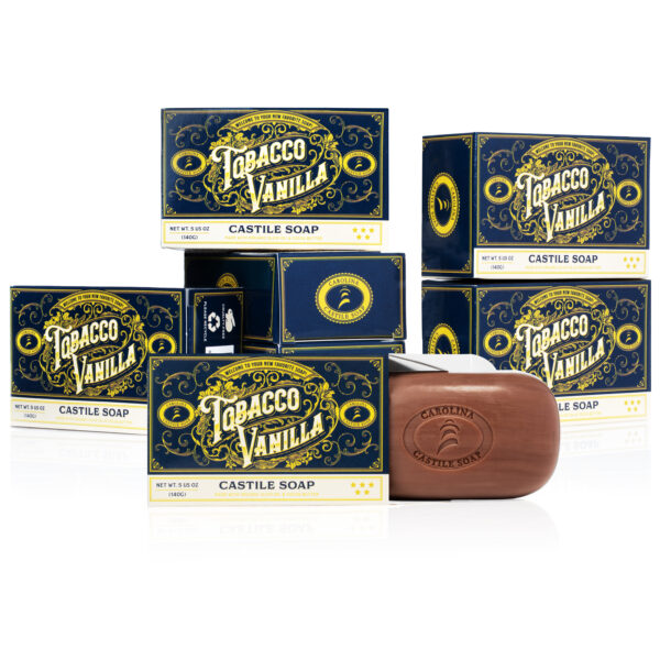 Arrangement of 6 bars of soap contained in its outer packaging. One bar is partially out of it’s carton packaging displaying a brown bar of soap with Carolina Castile Soap Logo.